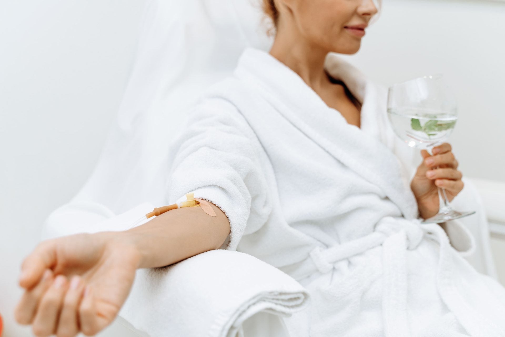 Woman in a white robe relaxing with an IV drip and a glass of water