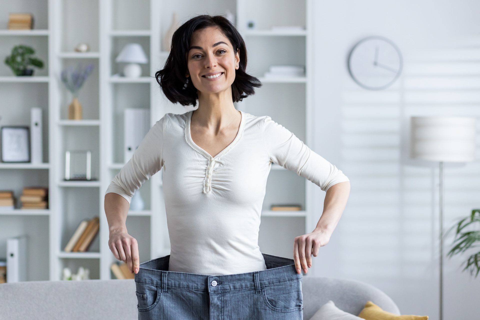 Smiling woman holding out her old, oversized jeans after weight loss