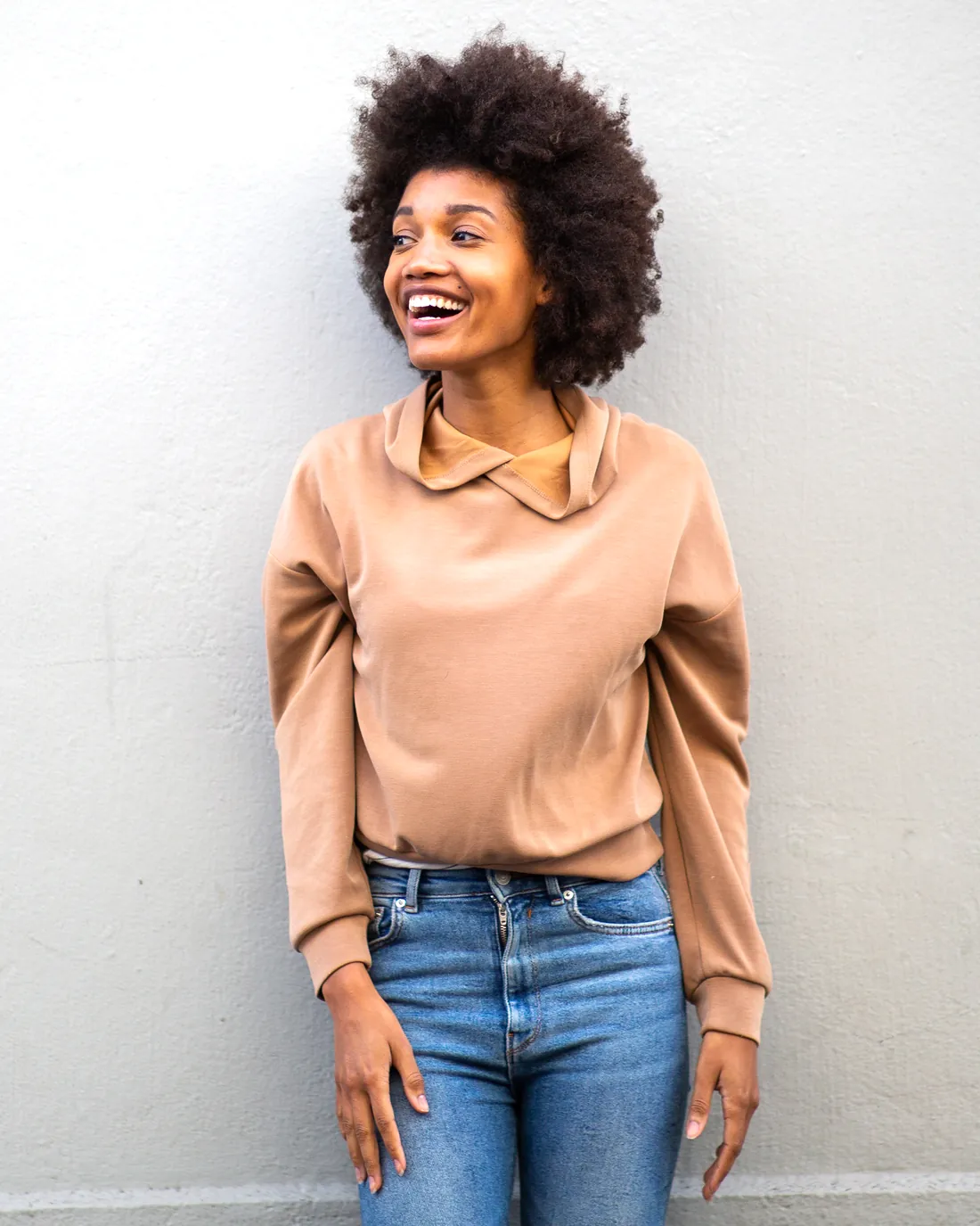 Homepage hero portrait (smiling woman by gray wall, final crop) Smiling woman with an afro hairstyle standing by a gray wall