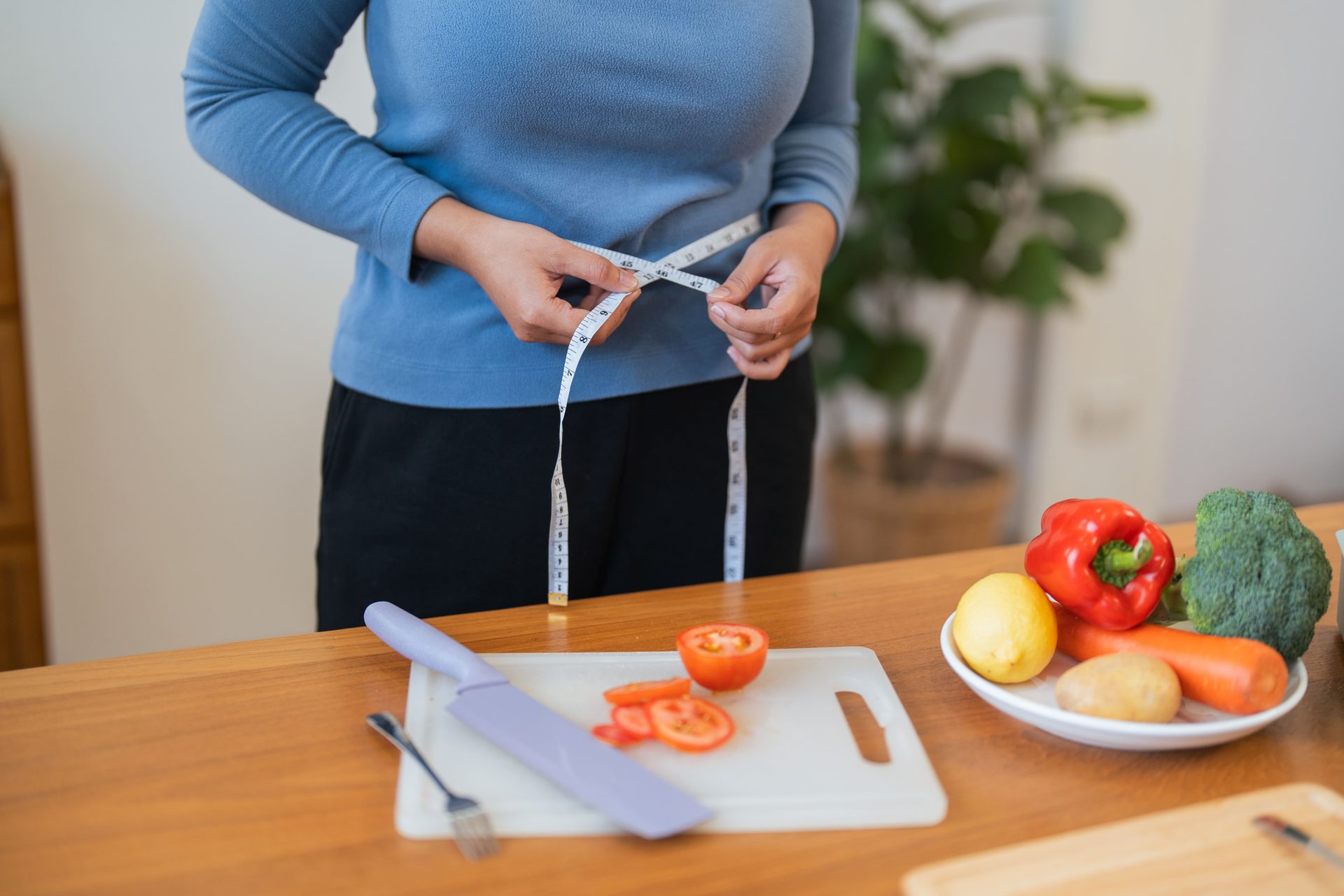 Woman measuring her waist next to fresh vegetables